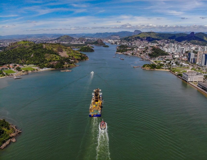 Vista aérea de Vitória, no Espírito Santo, com a orla portuária e um grande navio navegando pelo canal.