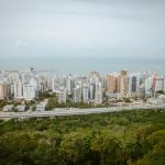 Vista aérea panorâmica da área urbana de Vitória, com edifícios, áreas verdes e faixa litorânea