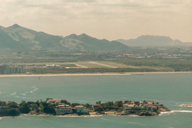 Vista aérea do litoral de Vitória, com áreas urbanas, mar e montanhas ao fundo.