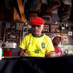 Homem idoso e menino criam uma peça artística juntos em uma oficina colorida no Brasil.