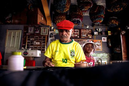 Homem idoso e menino criam uma peça artística juntos em uma oficina colorida no Brasil.