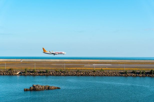 Avião comercial se aproxima de uma pista de pouso à beira-mar sob céu azul.