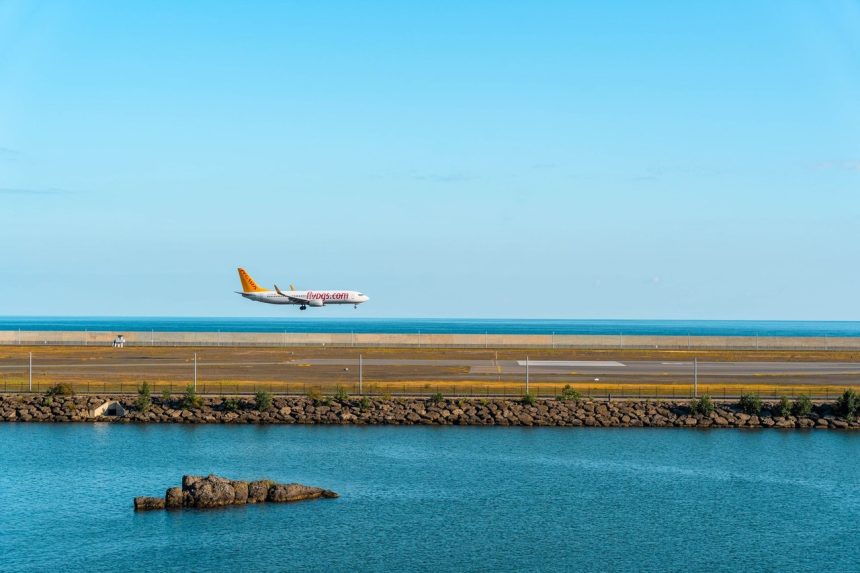 Avião comercial se aproxima de uma pista de pouso à beira-mar sob céu azul.