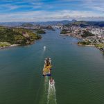 Vista aérea de Vitória com a orla urbana e um grande navio navegando pelo canal da baía.