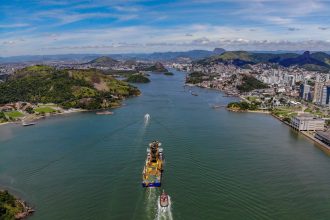 Vista aérea da orla de Vitória, com a área urbana junto ao canal e um navio em circulação.