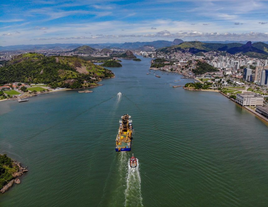 Vista aérea da orla de Vitória, com a área urbana junto ao canal e um navio em circulação.